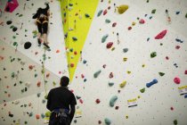 Treinador assistindo mulher enquanto escalava na parede artificial no ginásio — Fotografia de Stock