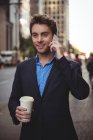 Бізнесмен розмовляє по мобільному телефону і тримає каву на вулиці — стокове фото