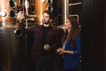 Uomo e donna che esaminano bottiglie in fabbrica di birra — Foto stock