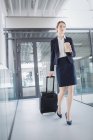 Businesswoman holding suitcase walking through office corridor — Stock Photo