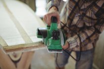 Mid-section of man using modified planer in the surfboard workshop — Stock Photo