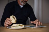 Homem usando tablet digital enquanto toma café da manhã em casa — Fotografia de Stock