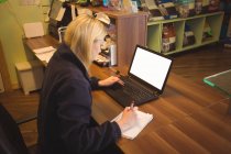 Жінка використовує ноутбук і пише на блокноті в офісі — стокове фото