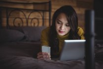 Frau liegt mit digitalem Tablet und Handy im heimischen Schlafzimmer — Stockfoto
