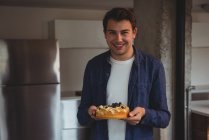 Uomo allegro che tiene la torta di mirtilli in soggiorno a casa — Foto stock