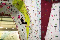 Femme pratiquant l'escalade sur mur d'escalade artificielle dans la salle de gym — Photo de stock