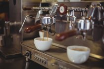 Primer plano del espresso que se vierte de la máquina de café en la cafetería - foto de stock