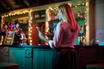 Hermosa camarera usando una tableta digital en el bar - foto de stock