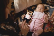 Mother taking baby photo on mobile phone indoors — Stock Photo