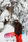 Чоловік стоїть і тримає сноуборд на снігу покритій горі — стокове фото