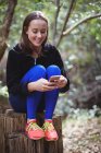 Усміхнена жінка використовує мобільний телефон у лісі — стокове фото