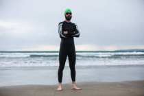 Portrait of athlete in wet suit standing with his hands crossed on the beach — Stock Photo