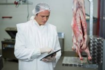 Male butcher maintaining records on digital tablet at meat factory — Stock Photo
