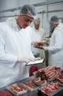 Male butcher maintaining records over digital tablet at meat factory — Stock Photo