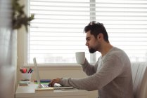 Людина використовує ноутбук, маючи каву вдома — стокове фото