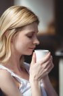 Beautiful woman smelling coffee in living room at home — Stock Photo