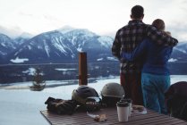 Vista trasera de la pareja abrazándose contra montañas cubiertas de nieve - foto de stock