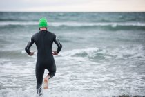 Vista trasera del atleta en traje de neopreno corriendo hacia el mar - foto de stock
