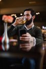 Чоловік тримає мобільний телефон і п'є в барі — стокове фото