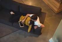 Веселая пара, лежащая вместе на диване с помощью цифрового планшета в гостиной — стоковое фото