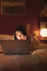 Жінка лежить і використовує ноутбук на ліжку в спальні — стокове фото