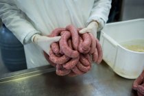 Milieu de la boucherie détenant des saucisses crues dans une usine de viande — Photo de stock