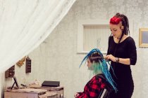 Beautician style clients hair in dreadlocks shop — стоковое фото