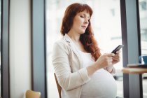 Беременная деловая женщина, использующая мобильный телефон в офисной столовой — стоковое фото