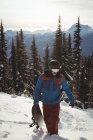 Чоловік, що йде зі сноубордом на снігу, покрив гору деревами — стокове фото