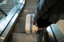 Femme d'affaires avec bagages descendant sur l'escalier roulant au terminal de l'aéroport — Photo de stock