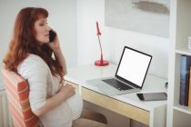 Беременная женщина разговаривает по мобильному телефону в кабинете дома — стоковое фото