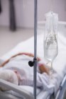 Крупним планом IV крапельна пляшка поруч з ліжком пацієнтів у лікарняній кімнаті — стокове фото