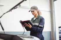 Meccanico femminile che utilizza un dispositivo diagnostico elettronico nel garage di riparazione — Foto stock