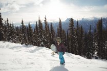 Frau hält im Winter Snowboard am Berg gegen Bäume — Stockfoto