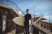 Thoughtful surfer standing with surfboard on beach — Stock Photo