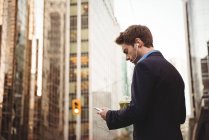 Бізнесмен слухає музику і використовує мобільний телефон, стоячи на вулиці — стокове фото