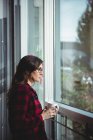 Thoughtful woman looking through window while having coffee in office — Stock Photo