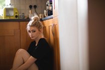Mujer pensativa sentada en la cocina en casa - foto de stock