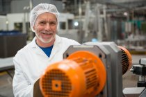 Retrato del trabajador masculino feliz parado por las máquinas en la fábrica de la bebida fría - foto de stock
