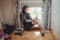 Frau sitzt auf Fensterbank und nutzt zu Hause digitales Tablet — Stockfoto