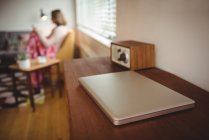 Ordenador portátil en la mesa de madera en la sala de estar con la mujer en el fondo en casa - foto de stock