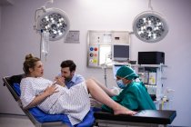 Medico esaminando donna incinta durante il parto mentre l'uomo le tiene la mano in sala operatoria — Foto stock