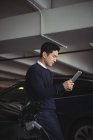 Uomo che utilizza tablet digitale durante la ricarica di auto elettriche in garage — Foto stock