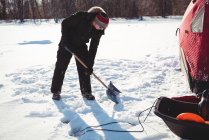 Ice fisherman digging with shovel in snowy landscape — Stock Photo