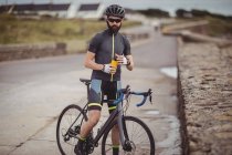 Atleta rinfrescante dalla bottiglia mentre guida in bicicletta su strada — Foto stock