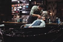 Close-up de lavatório com barbeiro barbear cliente em segundo plano na barbearia — Fotografia de Stock