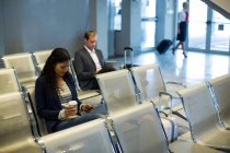 Comutador usando telefone celular na área de espera no terminal do aeroporto — Fotografia de Stock