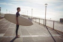Nachdenklicher Surfer steht mit Surfbrett auf Pier am Strand — Stockfoto