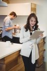 Женщина с помощью цифрового планшета в то время как мужчина работает на заднем плане на кухне — стоковое фото