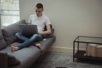 Чоловік використовує ноутбук на дивані у вітальні вдома — стокове фото